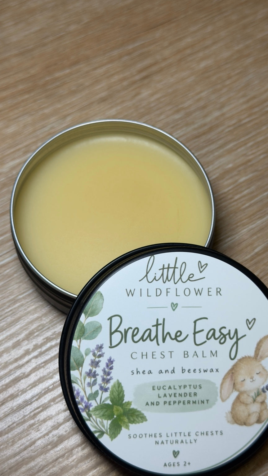 Open tin of Little Wildflower Breathe Easy Chest Balm beside its labeled lid.